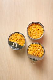 Open tin cans of sweet corn on wooden table, flat lay