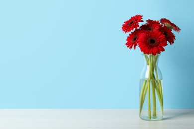 Photo of Bouquet of beautiful red gerbera flowers in glass vase on light blue background. Space for text