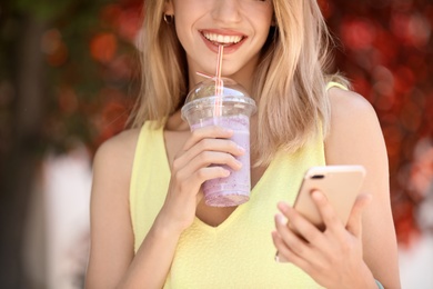 Young woman with plastic cup of healthy smoothie outdoors