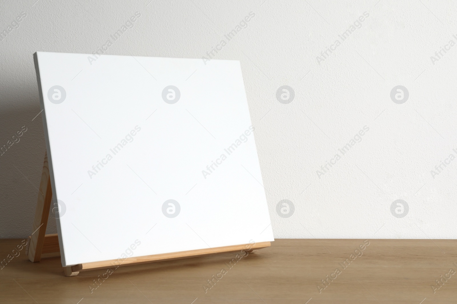 Photo of Wooden easel with blank canvas on table. Space for text