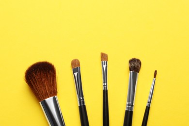Set of makeup brushes on yellow background, flat lay. Space for text