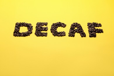 Word Decaf made of coffee beans on yellow background, space for text