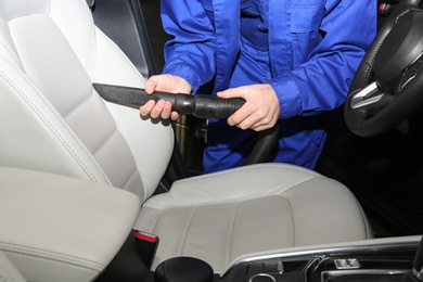 Closeup of worker vacuuming automobile seat, view from inside. Car wash service