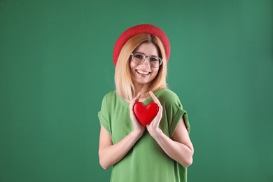 Portrait of beautiful woman holding decorative heart on color background