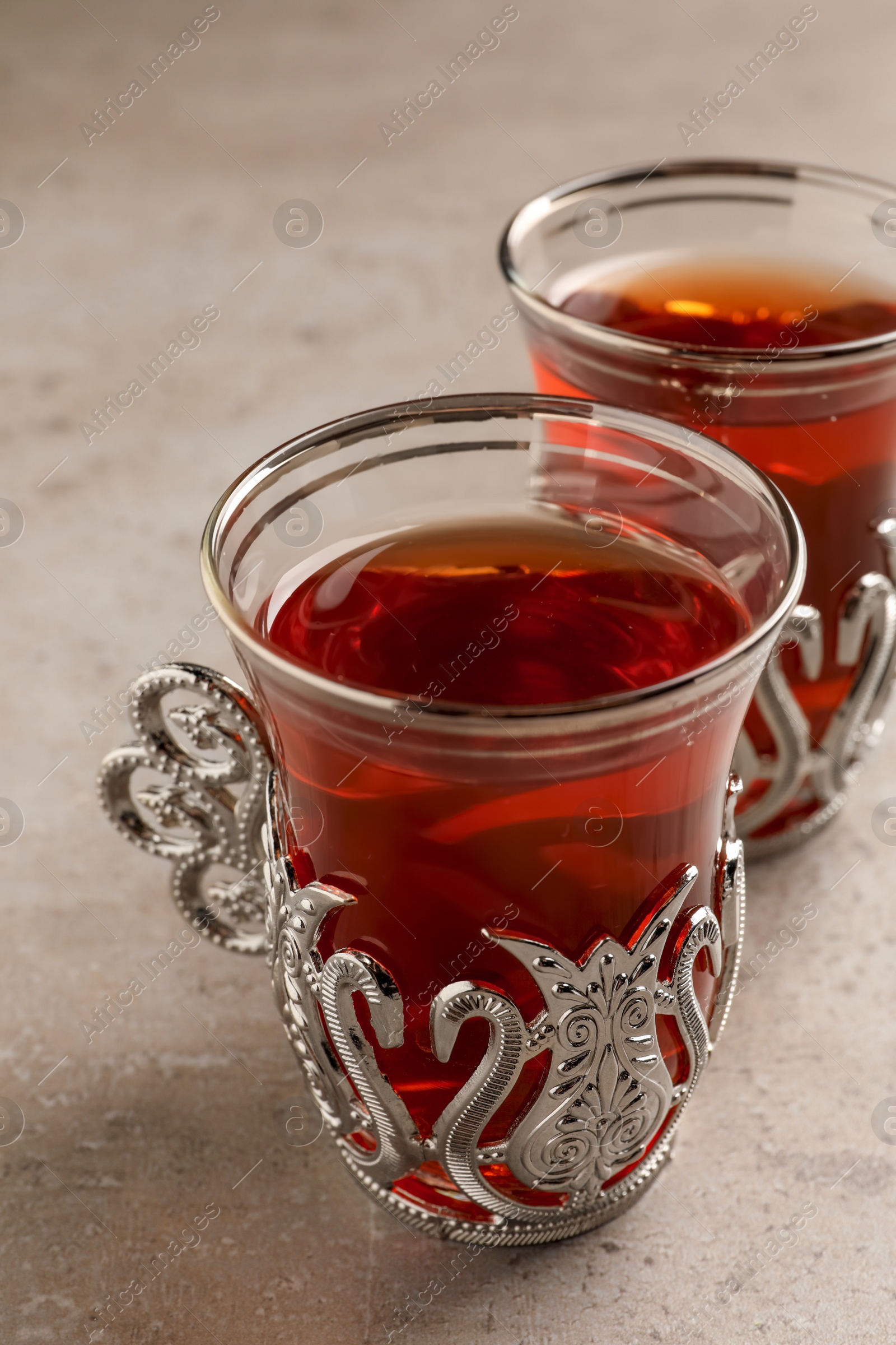 Photo of Glasses of traditional Turkish tea in vintage holders on light grey table, closeup