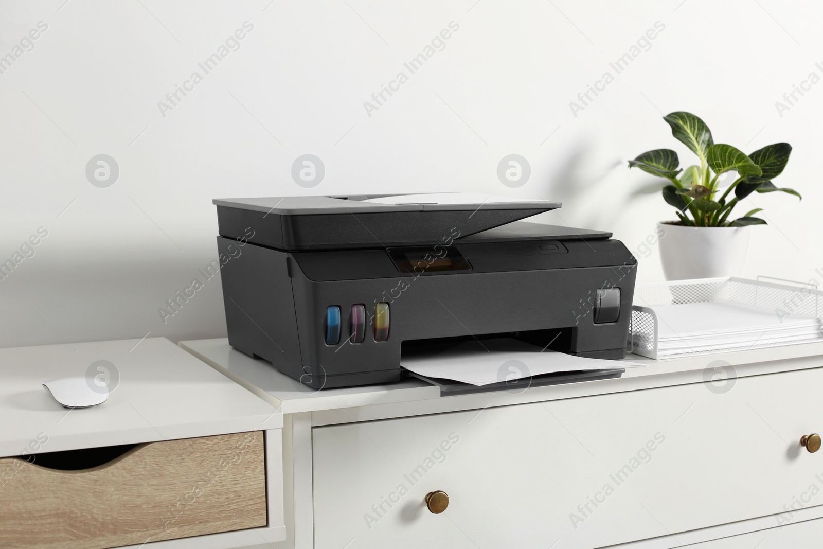Photo of Modern printer with paper on chest of drawers indoors