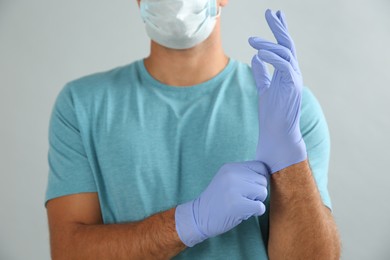 Photo of Man in protective face mask putting on medical gloves against grey background, closeup