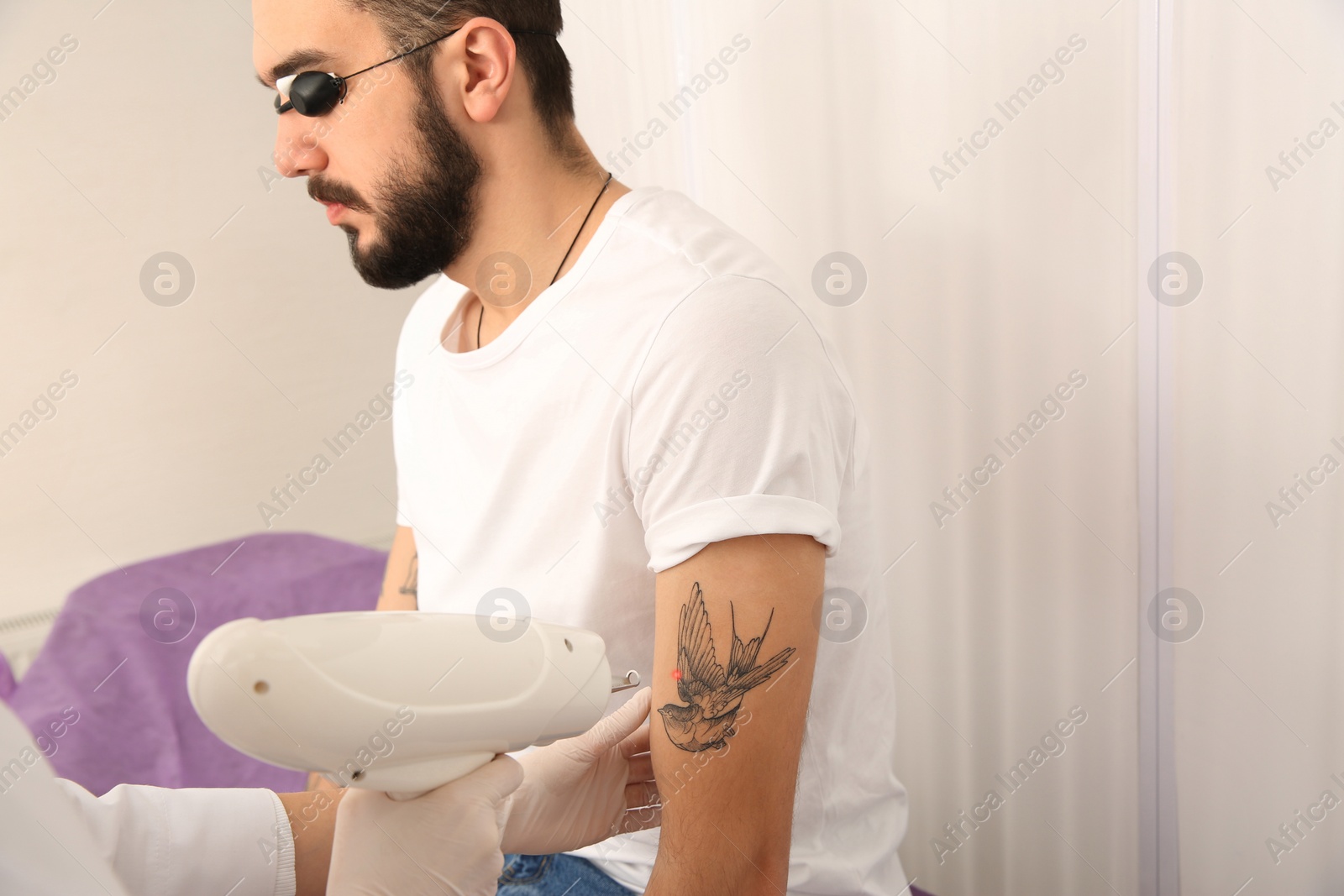 Photo of Young man undergoing laser tattoo removal procedure in salon