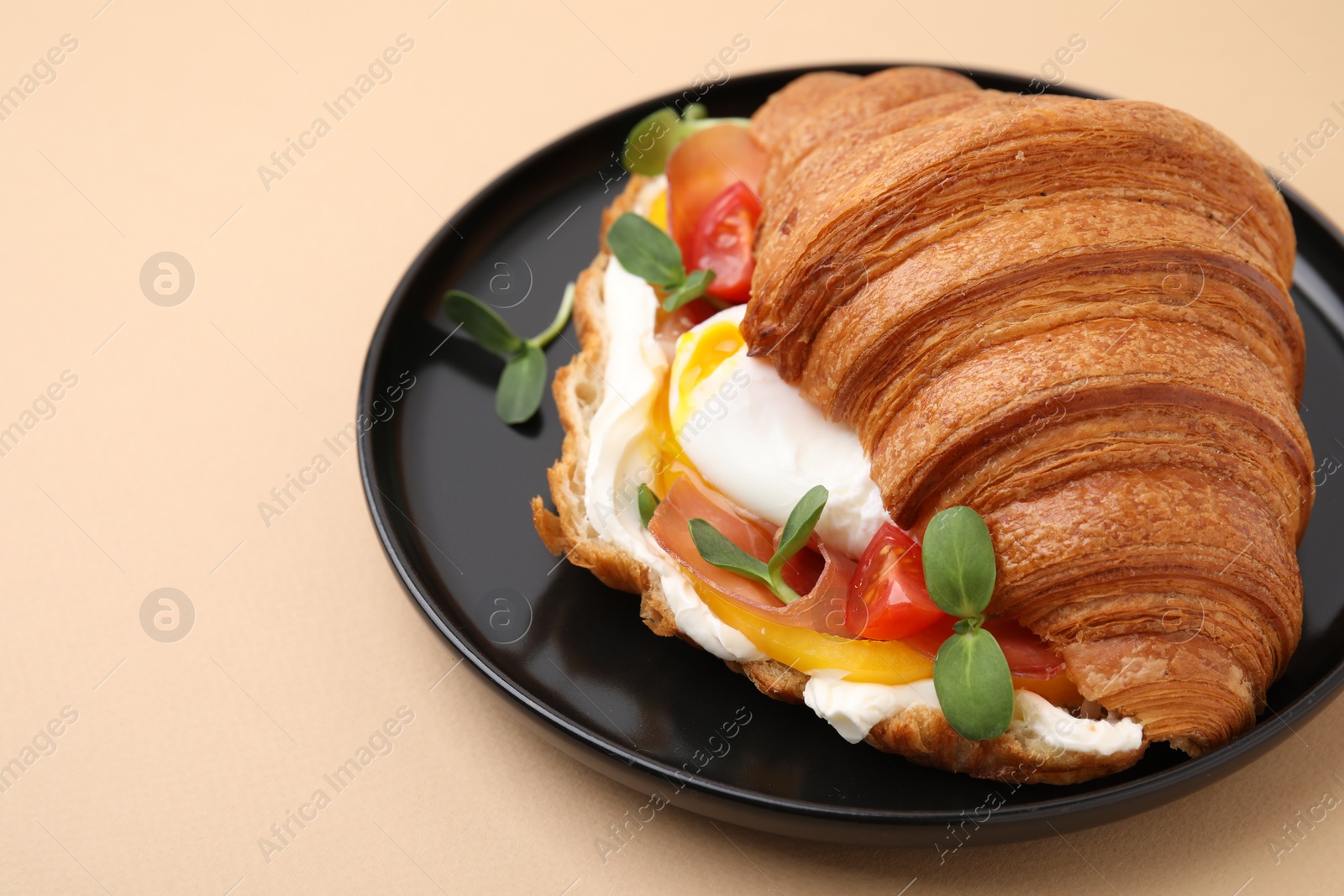 Photo of Tasty croissant with fried egg, tomato and microgreens on beige background, closeup