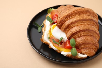 Tasty croissant with fried egg, tomato and microgreens on beige background, closeup