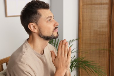 Photo of Man with clasped hands praying in room at home