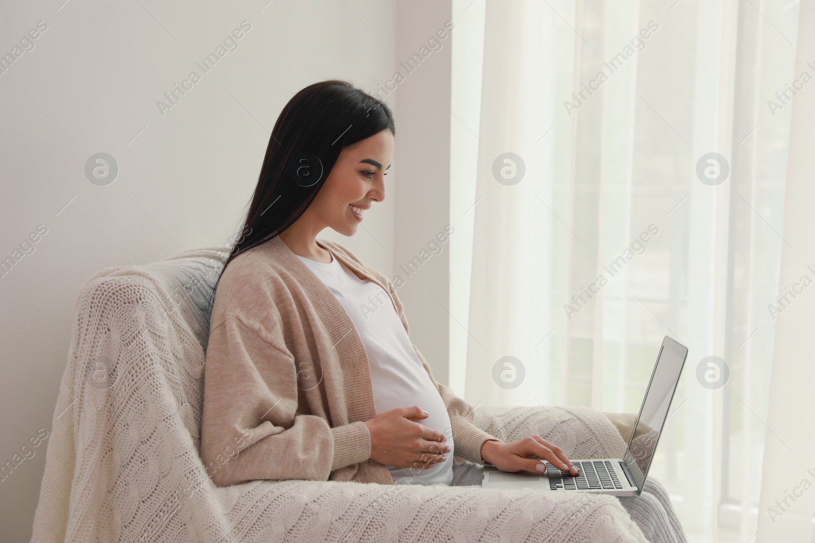 Photo of Pregnant young woman with laptop at home, space for text