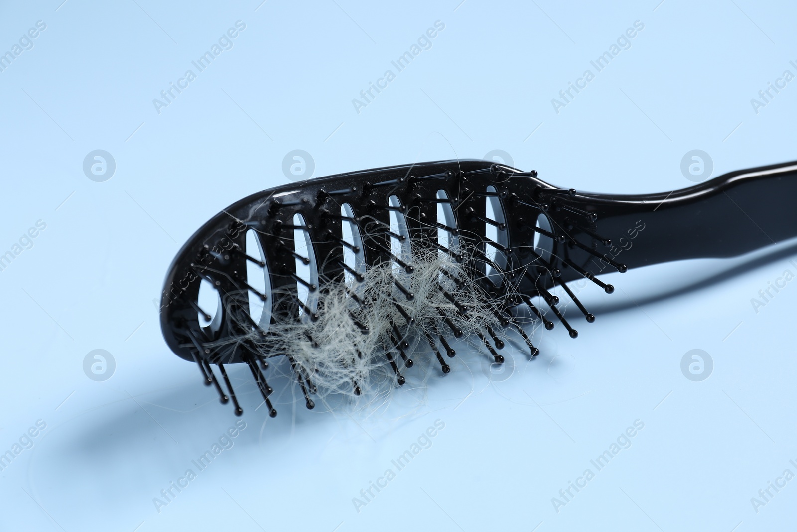 Photo of Brush with lost hair on light blue background, closeup