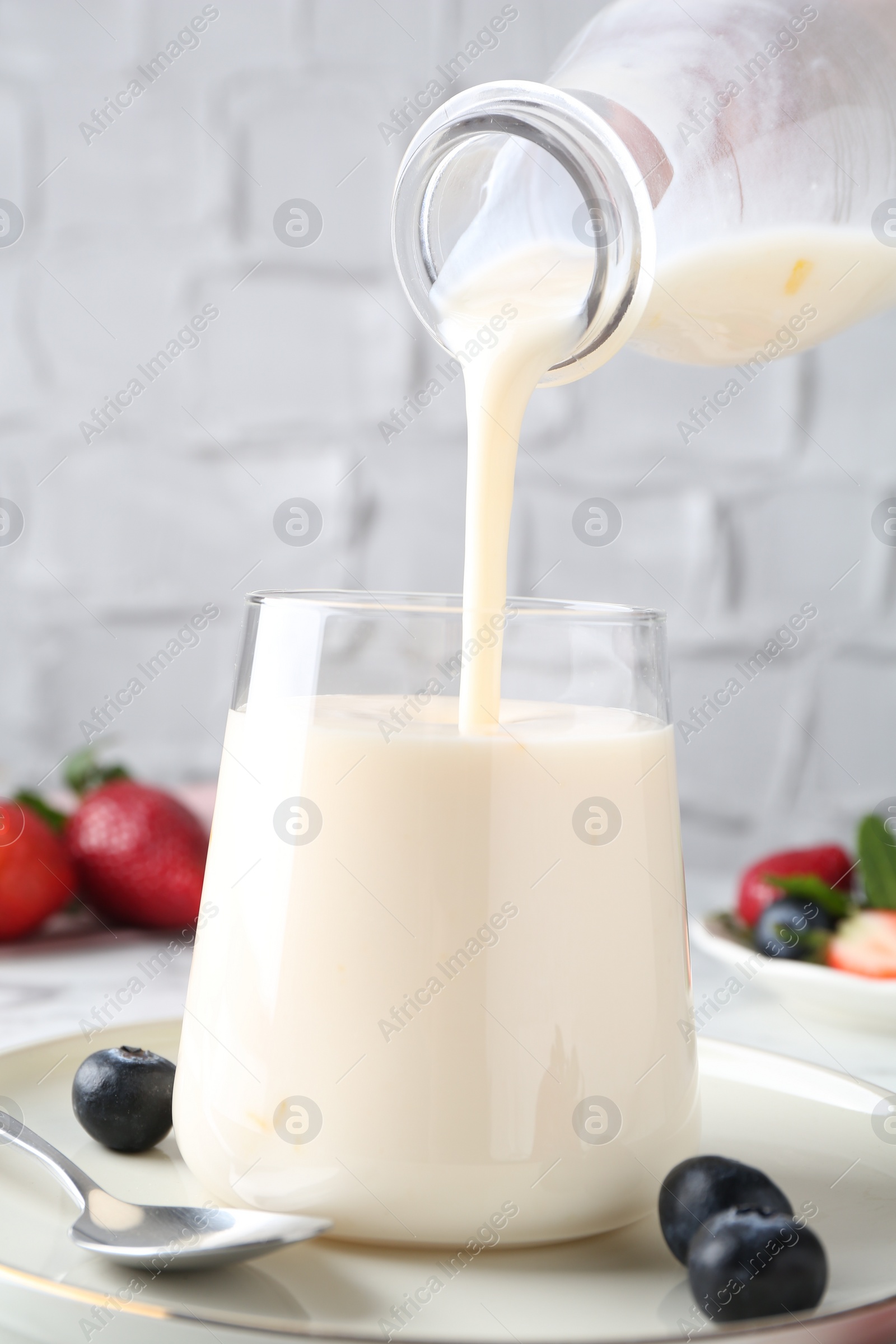 Photo of Pouring tasty yogurt into glass at table, closeup
