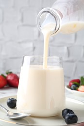 Pouring tasty yogurt into glass at table, closeup