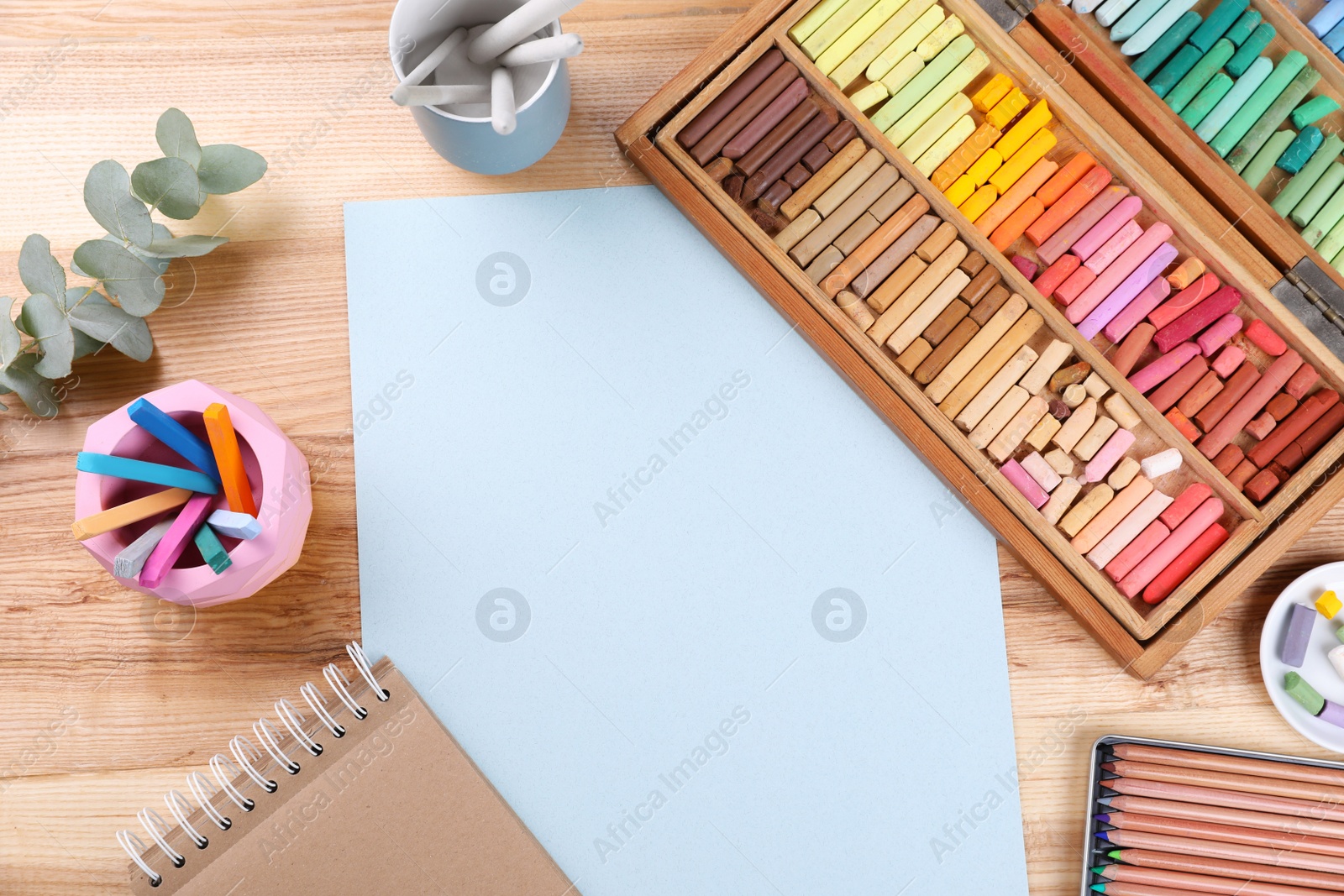 Photo of Layout with blank paper, soft pastels and other drawing supplies on wooden table at artist's workplace, top view. Space for design