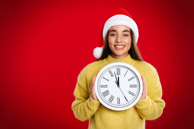 Photo of Woman in Santa hat with clock on red background, space for text. Christmas countdown