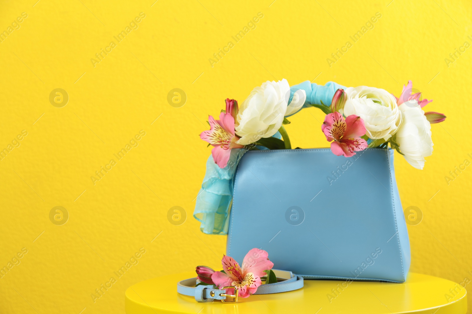 Photo of Elegant handbag with flowers and belt on table against yellow background, space for text