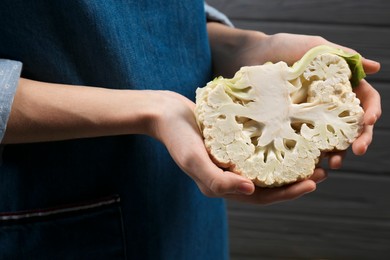 Photo of Woman holding fresh cauliflower against black wooden wall, closeup