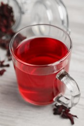 Delicious hibiscus tea and dry flowers on white wooden table, closeup