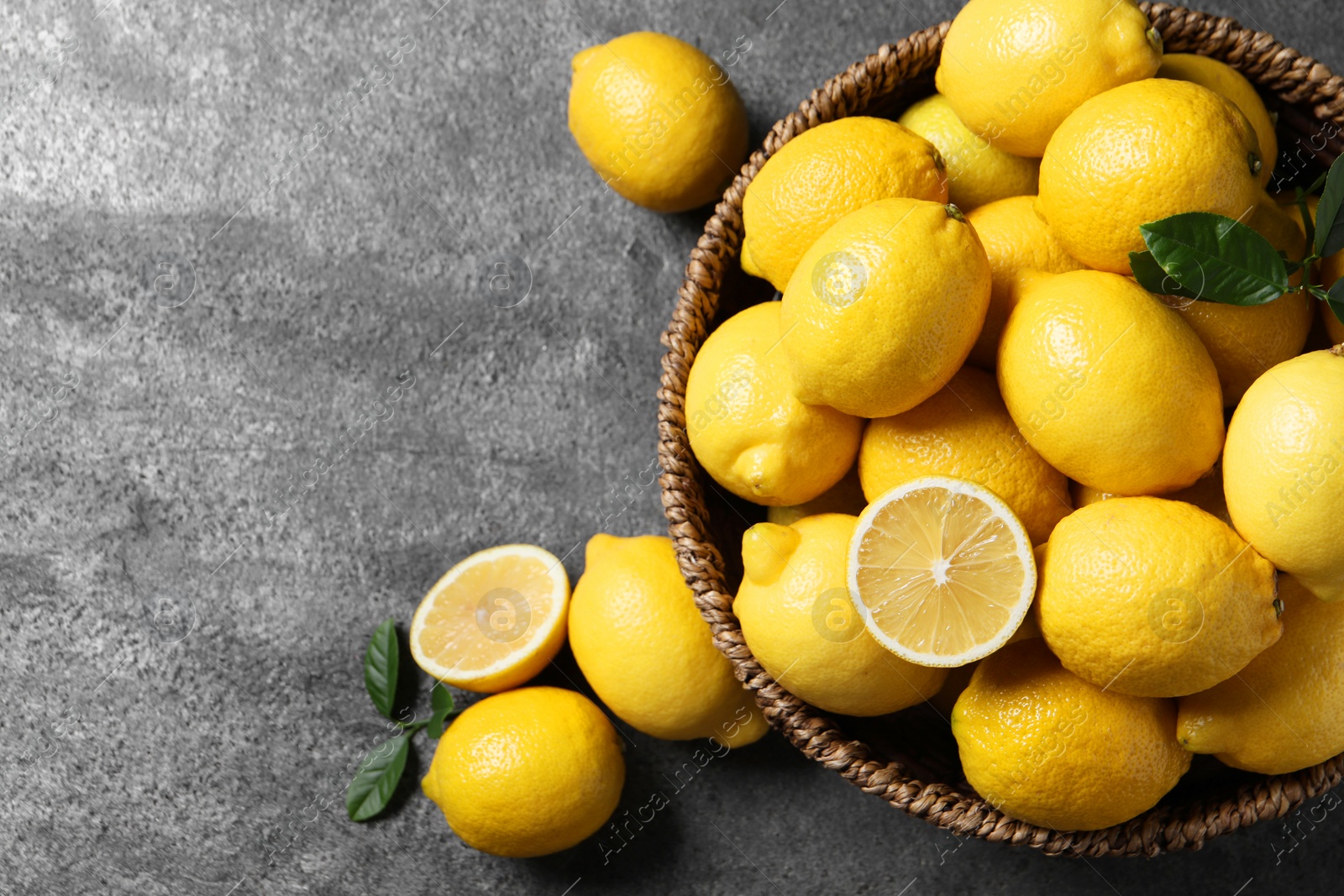 Photo of Fresh lemons in wicker basket on grey table, top view. Space for text