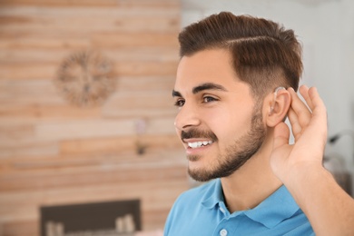 Young man with hearing aid indoors. Space for text