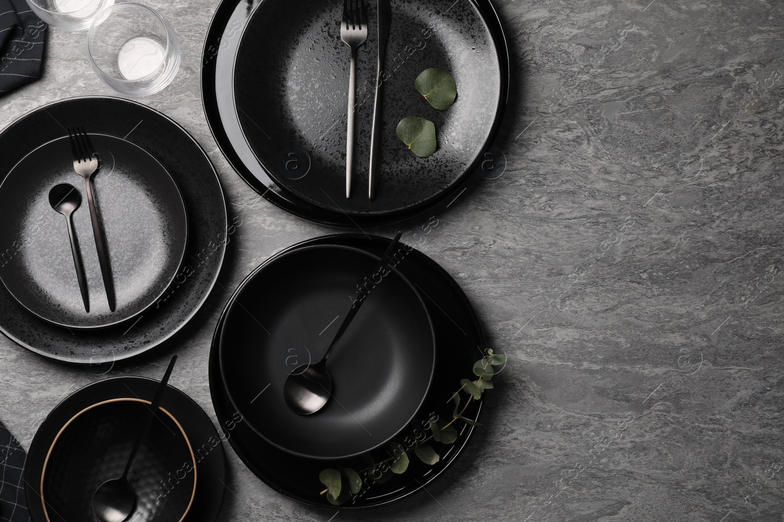 Photo of Stylish table setting. Dishes, cutlery and eucalyptus branch on grey surface, flat lay with space for text