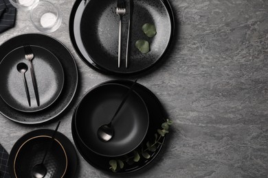 Photo of Stylish table setting. Dishes, cutlery and eucalyptus branch on grey surface, flat lay with space for text