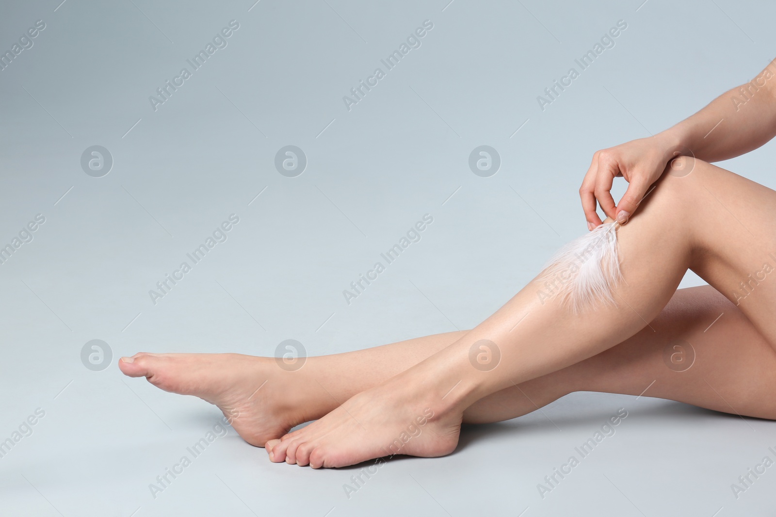 Photo of Closeup of woman touching leg with feather on grey background, space for text. Epilation procedure