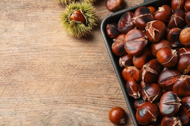 Photo of Delicious roasted edible chestnuts on wooden table, flat lay. Space for text