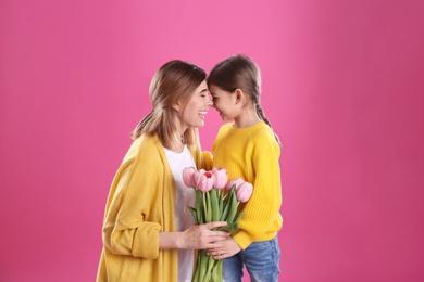 Happy mother and daughter with flowers on color background. International Women's Day