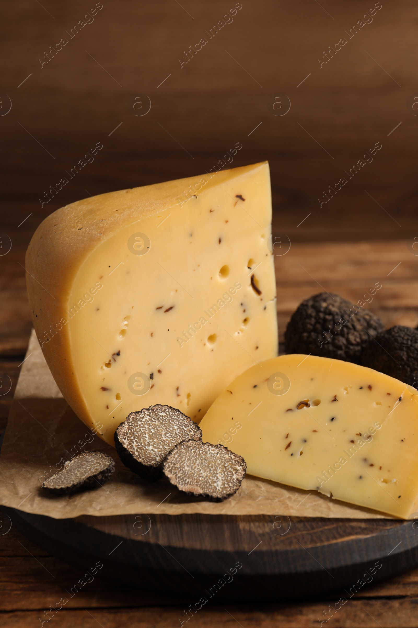 Photo of Board with delicious cheese and fresh black truffles on wooden table