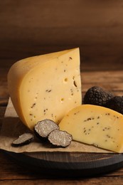 Photo of Board with delicious cheese and fresh black truffles on wooden table