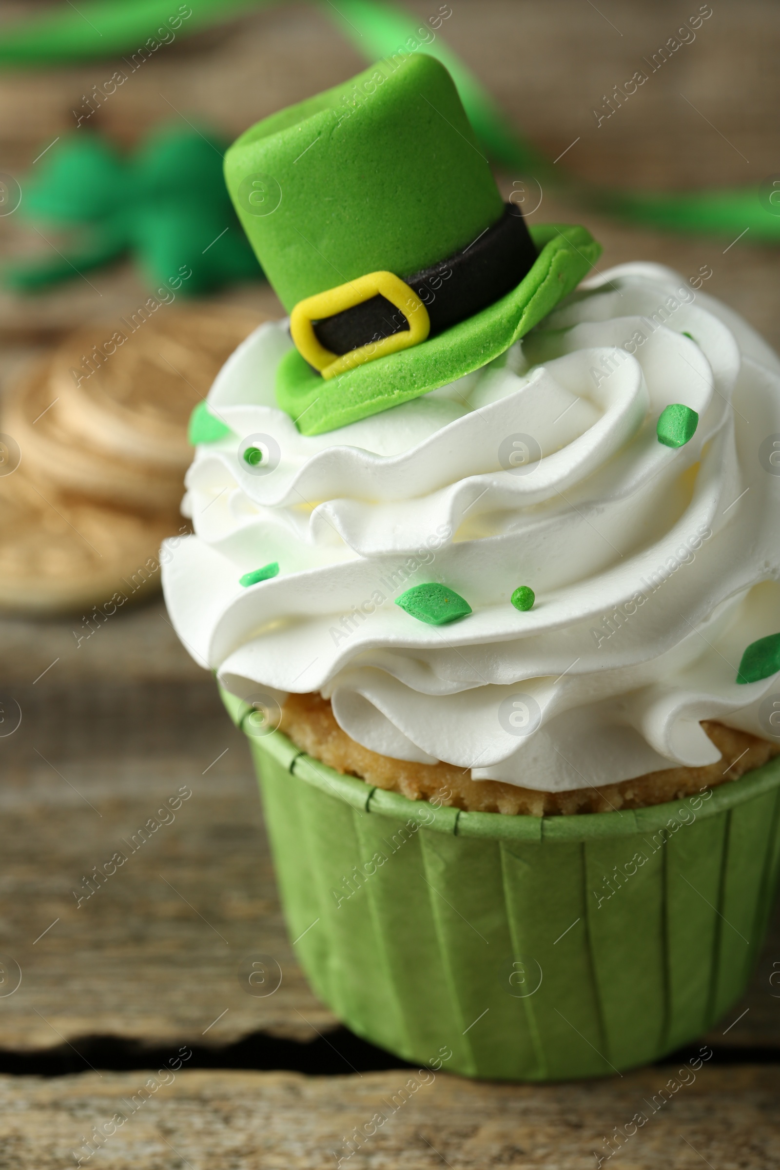 Photo of St. Patrick's day party. Tasty cupcake with green leprechaun hat topper on wooden table, closeup