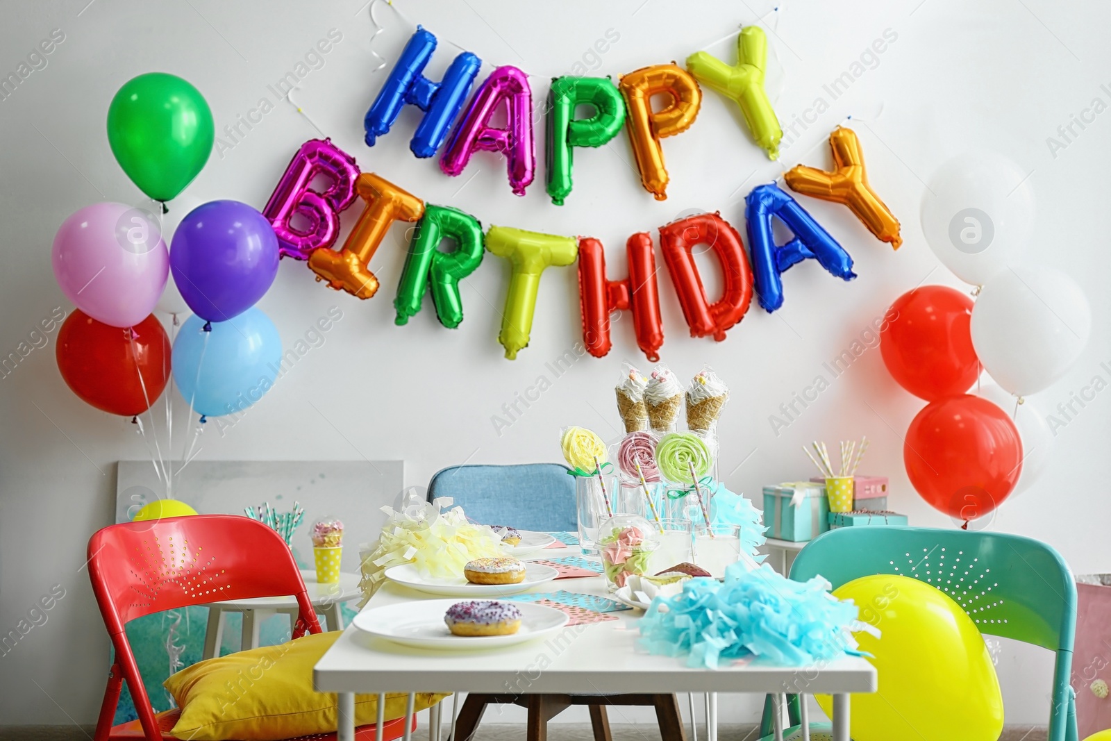 Photo of Table with treats and phrase HAPPY BIRTHDAY made of colorful balloon letters in living room