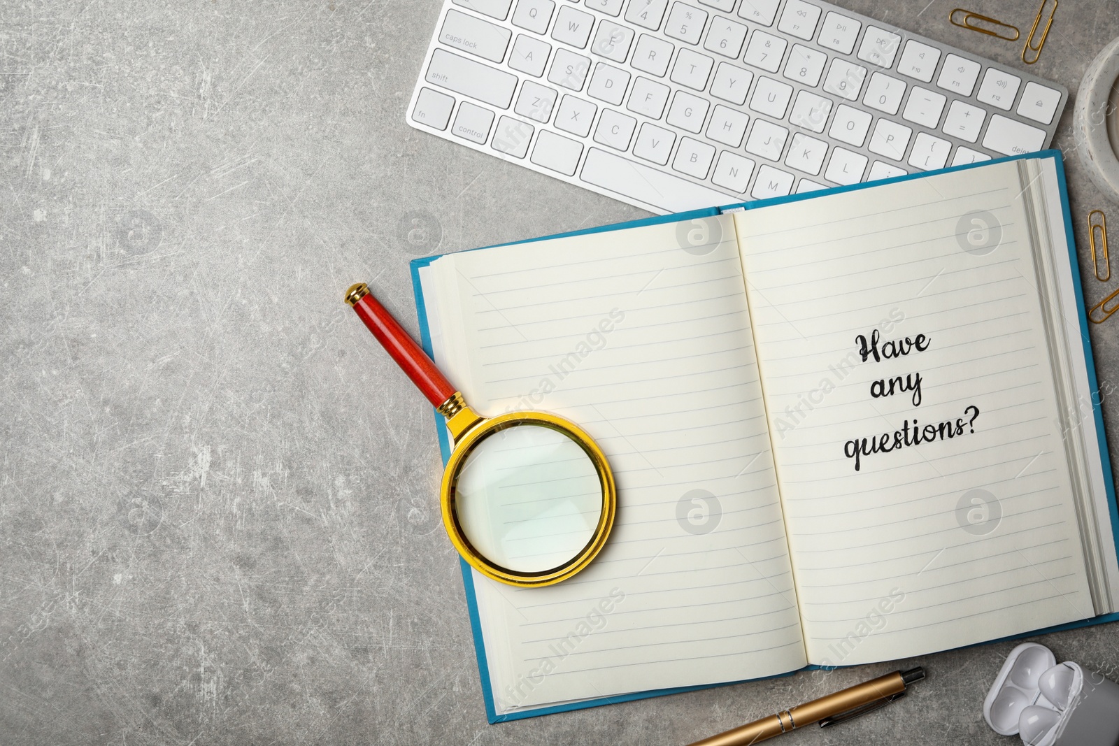 Photo of Notebook with phrase HAVE ANY QUESTIONS and magnifying glass on grey stone table, flat lay