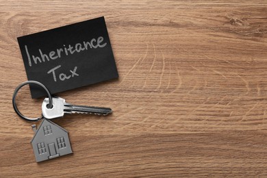 Photo of Inheritance Tax. Card and key with key chain in shape of house on wooden table, flat lay. Space for text