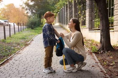 Photo of Young mom giving school backpack to her son outdoors
