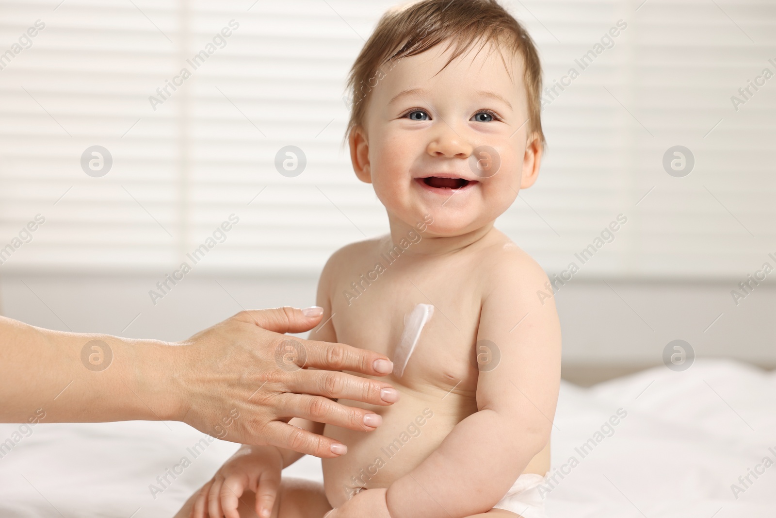 Photo of Mother applying body cream onto baby`s skin at home