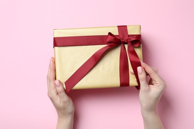 Christmas present. Woman holding gift box on pink background, top view