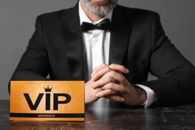 Photo of Man sitting at table with VIP sign on grey background, closeup