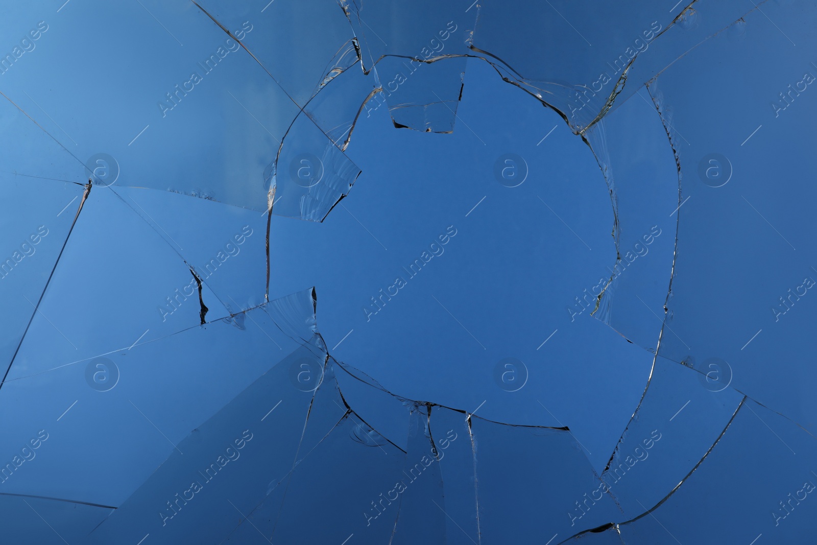 Photo of Closeup view of broken glass with cracks on blue background