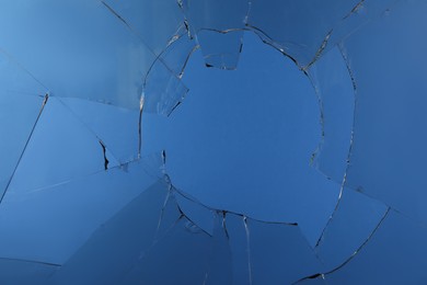 Photo of Closeup view of broken glass with cracks on blue background