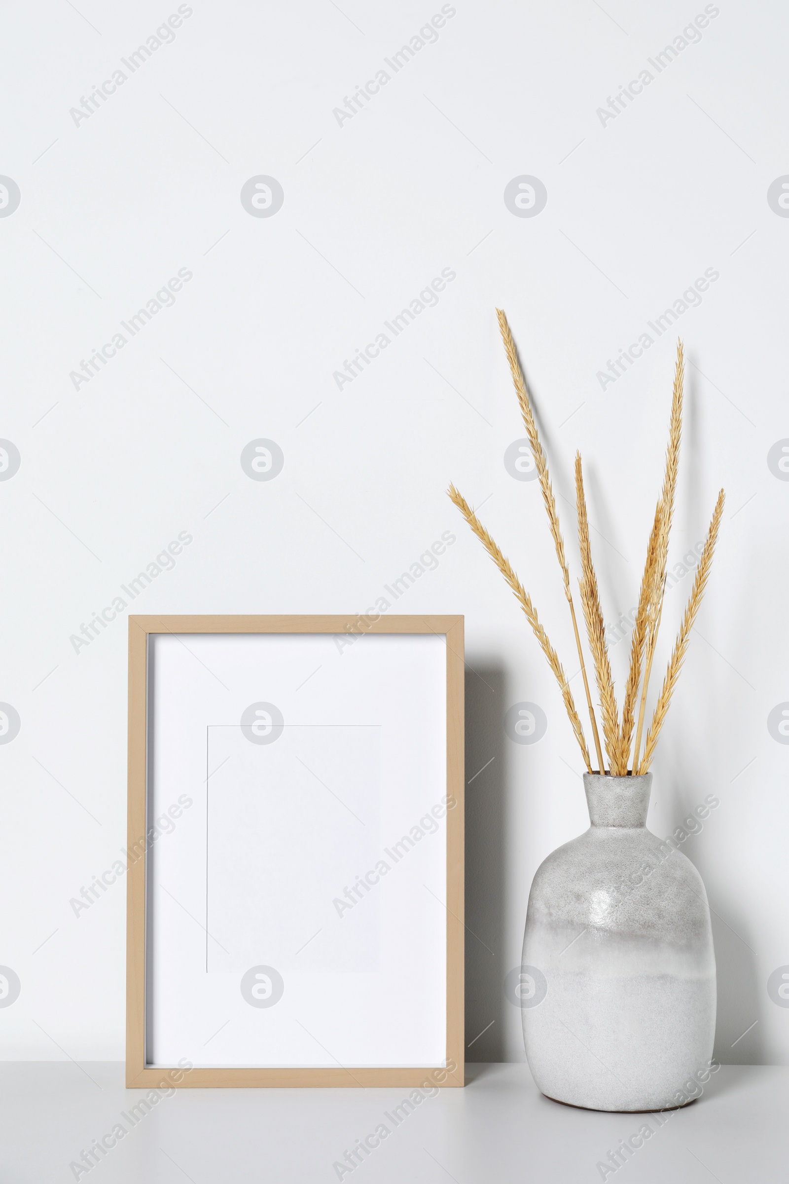 Photo of Empty photo frame and vase with dry decorative spikes on white table. Mockup for design