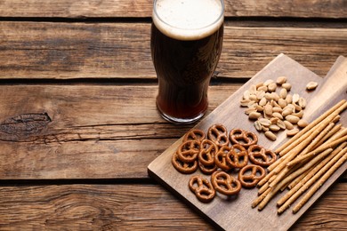 Photo of Glass of beer served with delicious pretzel crackers and other snacks on wooden table. Space for text