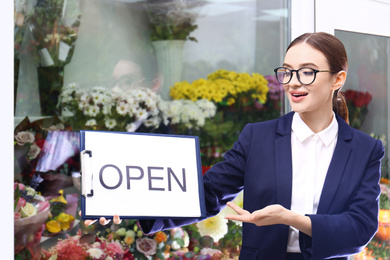 Female business owner holding OPEN sign near flower shop