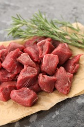 Photo of Pieces of raw beef meat and rosemary on grey textured table, closeup