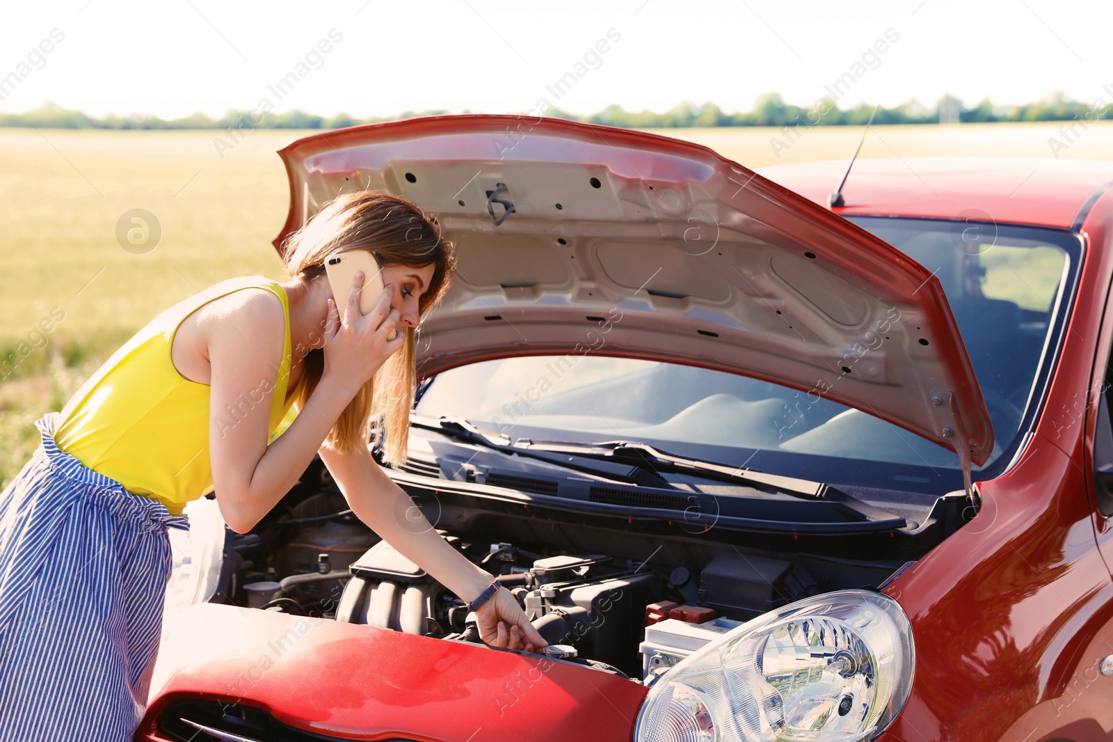 Photo of Stressed woman with mobile phone standing near broken car in countryside