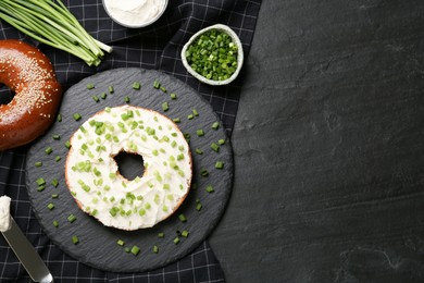 Photo of Delicious bagel with cream cheese and green onion on black table, flat lay. Space for text