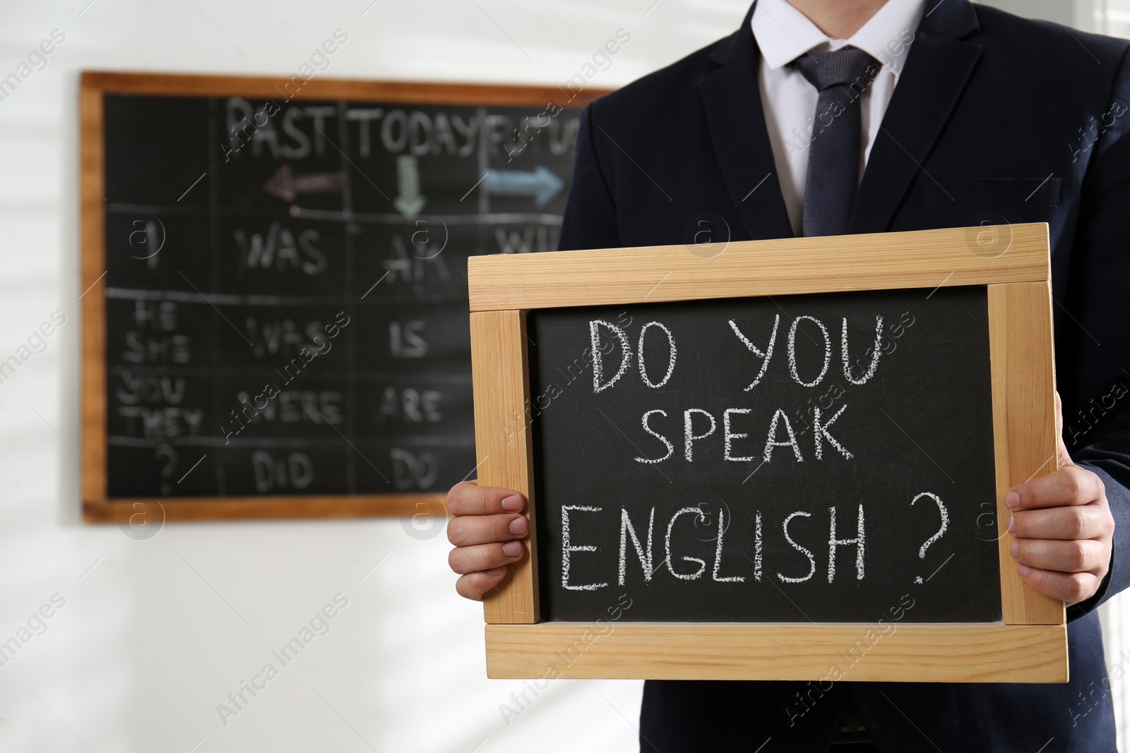 Photo of Teacher holding small chalkboard with inscription Do You Speak English? in classroom, closeup